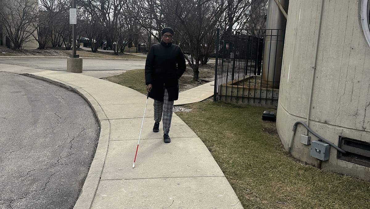 Mariama walking along a sidewalk with her white cane