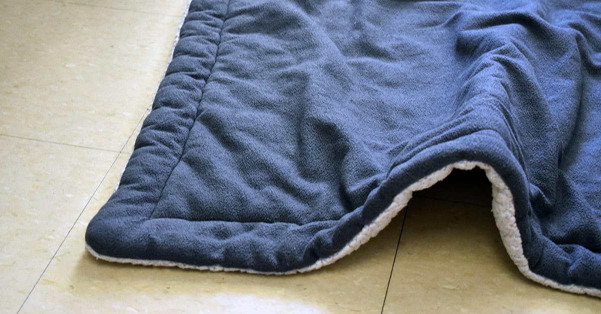 A blue blanket is not laying flat on the floor, becoming a potential tripping hazard.
